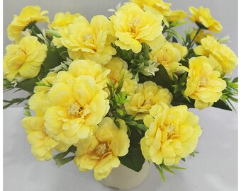 May include: A bouquet of yellow artificial flowers with green leaves. The flowers are arranged in a white vase.