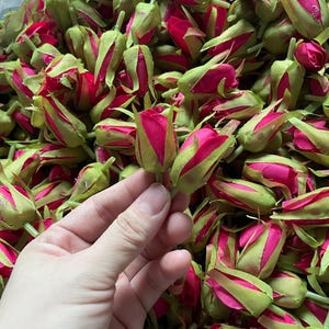 May include: A large pile of artificial rose buds in shades of pink and green. The buds are made of fabric and have a realistic appearance.