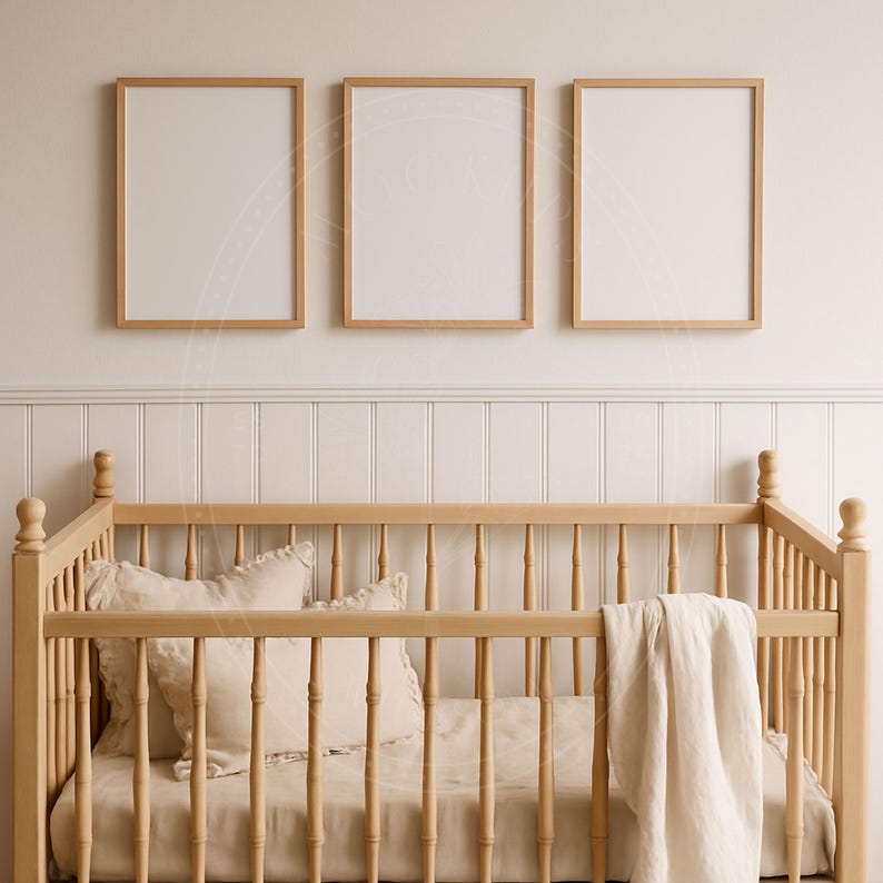 May include: A light wood baby crib with a cream-colored blanket and pillows. Three framed prints with light wood frames hang above the crib. The wall behind the crib is white with vertical paneling.