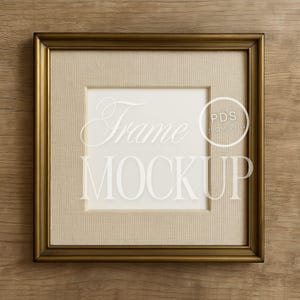 Puede incluir: Marco de fotos cuadrado dorado con un paspartú beige y un centro blanco. El marco tiene las palabras "Frame MOCKUP" en una fuente de escritura. El fondo es una superficie de madera.