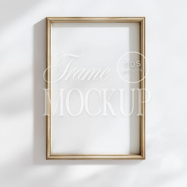 May include: A rectangular gold frame mockup against a white wall. The frame has a thin profile and a glossy finish. The words "Frame MOCKUP" are displayed in a stylized font within the frame. The image also includes the text "PDS JPG & PNG".