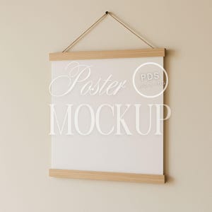 May include: A white poster mockup hanging on a beige wall with a wooden frame. The poster is blank and ready for your design. The text "Poster Mockup" is printed on the poster.
