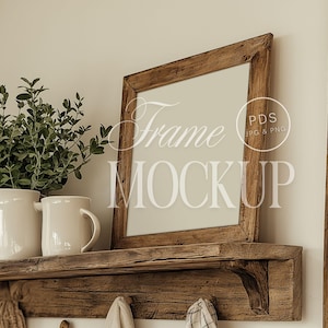 May include: A rustic wooden shelf with a brown wood frame mockup, two white ceramic mugs, and a green plant in a white pot. The shelf has a bracket on the right side and is mounted on a white wall. The frame mockup has the text "Frame Mockup" and "PDS JPG & PNG" on it.