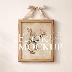 May include: A framed print with a watercolour illustration of a rabbit holding flowers. The artwork is in a wooden frame, suspended by a beige ribbon. The words "Frame MOCKUP" are printed on the image.