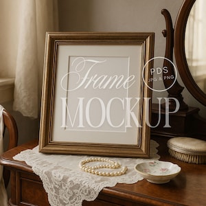 May include: A gold-framed picture frame mockup with the text "Frame MOCKUP" in white. The frame sits on a wooden surface with a lace doily, a pearl necklace, and a small decorative dish.