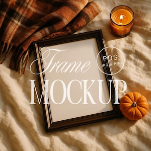 May include: A dark brown rectangular frame mockup with the word "Frame" and "MOCKUP" in white script. A small orange pumpkin, a lit candle in a glass jar, and a brown and orange plaid scarf are also in the image.
