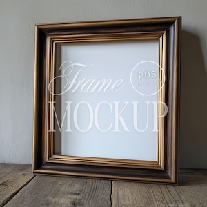 May include: A square picture frame with a dark brown wood finish and a gold trim. The frame is sitting on a wooden surface.