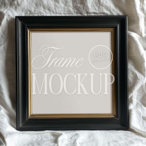 May include: Black picture frame with a gold inner border. The frame is sitting on a white fabric surface. The text "Frame Mockup" and "PDS JPG & PNG" is visible in the frame.