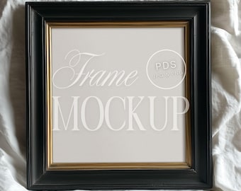 May include: Black picture frame with a gold inner border. The frame is sitting on a white fabric surface. The text "Frame Mockup" and "PDS JPG & PNG" is visible in the frame.