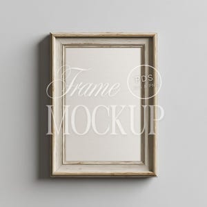 Puede incluir: Un marco de imagen de madera blanca con un paspartú marrón claro. El marco está en una pared gris claro. El texto "Frame Mockup" es visible en la imagen.