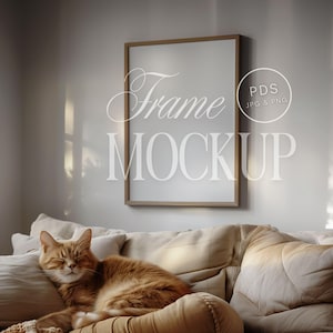 Op de afbeelding: Een beige bank met een bruine kat die slaapt op een kussen. Een gouden lijst met een witte passe-partout hangt aan de muur boven de bank. De tekst "Frame Mockup" staat in wit op de muur.