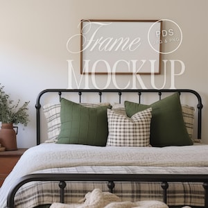 May include: A black metal bed frame with a white headboard and a brown wooden frame. The bed is made with a white and gray patterned quilt and green and white patterned pillows. The headboard has a blank frame hanging above it with the text "Frame Mockup" written below it.