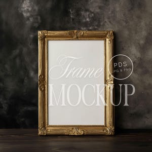 May include: A gold-colored ornate picture frame with a white background. The frame is sitting on a dark wooden surface.