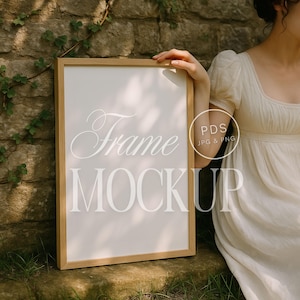 Puede incluir: Una maqueta de marco de madera con las palabras "Frame Mockup" en escritura blanca. El marco lo sostiene una persona que lleva un vestido blanco. El fondo es una pared de piedra con vides verdes.