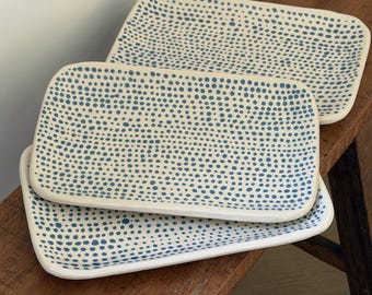 May include: Two rectangular ceramic trays with rounded corners, featuring an off-white base color decorated with a dense pattern of small, hand-painted blue dots distributed across the entire surface of each piece.