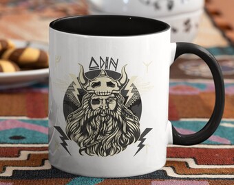 May include: White ceramic mug with a black rim and handle. The mug features a black and white illustration of a Viking warrior with a beard and horns. The text "Odin" is printed above the warrior's head.