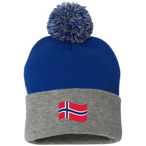 May include: A blue and gray knit beanie with a pom pom on top. The beanie has a Norwegian flag on the lower portion.
