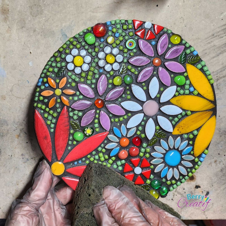 Work in progress of a mosaic kit, this image shows the black grout being wiped away using a damp cloth revealing the bright flower mosaic underneath