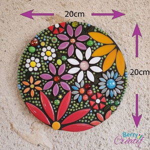 Flower mosaic artwork in bright colors hanging on a stone wall with measurements indicating its 20cm size