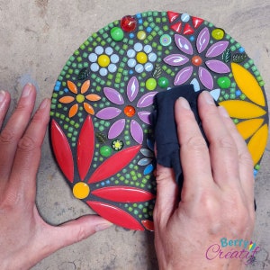 Circular flower mosaic kit is dry, and a clean cotton cloth is wiping off any excess back grout from the surface of the ceramic mosaic tiles