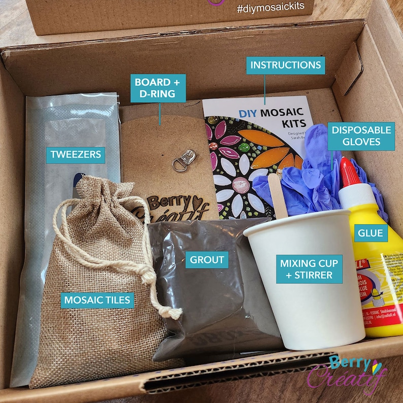 An open cardboard box showing the neat contents inside, there is an MDF board etched with the design, a papercup and mixer, a bottle of branded pva glue, a plastic selaed bag of powdered grout, written instructions, a bag of mosaic tiles and tweezers