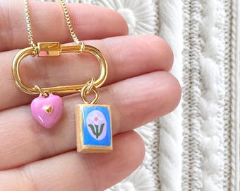 Utvalt karbinhalsband med en elegant, handgjord berlock i kombination med små olika guldfärgade berlocker.