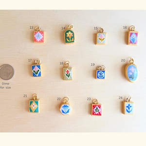 May include: A collection of twelve small gold-toned metal charms with colorful enamel floral and geometric designs, numbered 13 through 24. A US dime is included for scale, labeled as Dime for size, next to the charms arranged in three rows.