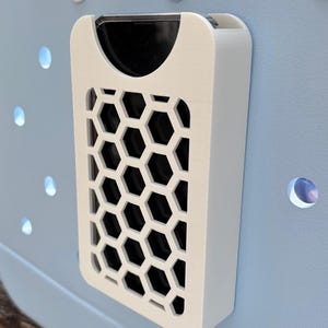 May include: A white rectangular object with a honeycomb pattern on a light blue surface. The object has a black interior and is mounted on a blue surface with circular cutouts and white circular accents.