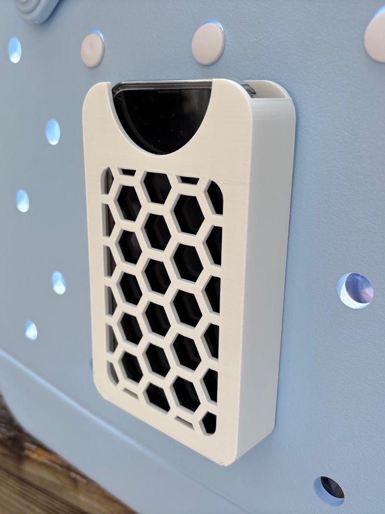 May include: A white rectangular object with a honeycomb pattern on a light blue surface. The object has a black interior and is mounted on a blue surface with circular cutouts and white circular accents.