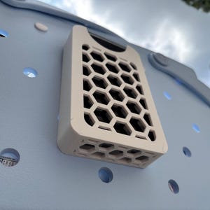 May include: A light blue tote bag with a white, rectangular, honeycomb-patterned attachment. The bag has several circular cutouts. The attachment is mounted on the side of the bag.