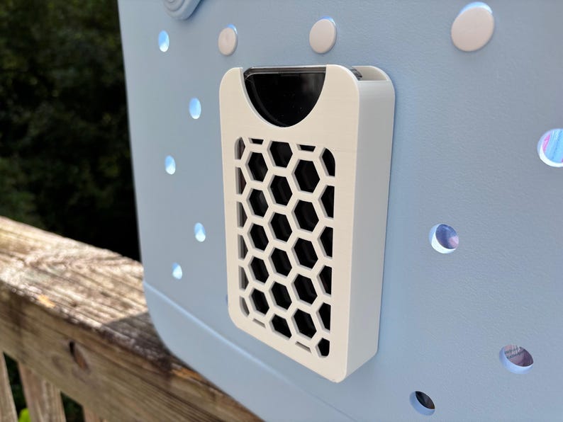 May include: A light blue tote bag with a white, honeycomb-patterned accessory attached. The accessory has a black interior and is mounted on the bag's exterior. The bag features several round, white accents and circular cutouts.
