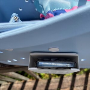 May include: A light blue plastic organizer with a built-in phone holder. The organizer has a curved design with several small holes and white circular feet. A small blue bag and a silver zipper pouch are visible inside.
