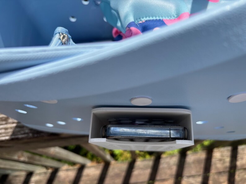 May include: A light blue plastic organizer with a built-in phone holder. The organizer has a curved design with several small holes and white circular feet. A small blue bag and a silver zipper pouch are visible inside.