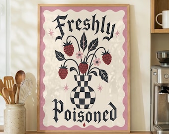 Op de afbeelding: Een rechthoekige wandkunstprint in een houten lijst met een zwart-wit geblokte vaas gevuld met donkerrode frambozen en kleine roze bloemen. De tekst Freshly Poisoned staat in een zwart gotisch lettertype boven en onder de vaas gedrukt.