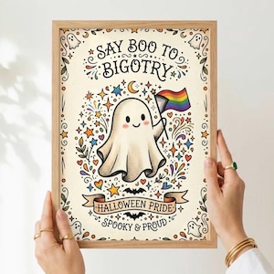 Può includere: Una stampa rettangolare incorniciata con un fantasma centrale che tiene in mano una bandiera progress pride. Il testo recita "SAY BOO TO BIGOTRY", "HALLOWEEN PRIDE" e "SPOOKY & PROUD". Il design include stelle colorate, piccoli fantasmi e pipistrelli su uno sfondo color crema.