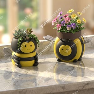May include: Two bee-shaped planters, one with succulents and the other with colorful flowers. The planters are yellow and black with smiling faces and grey wings. The planters are on a light-coloured surface.