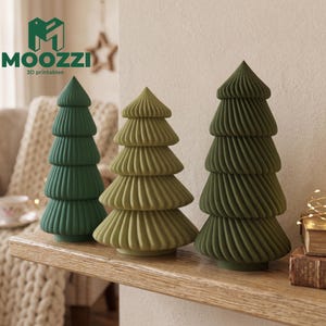 May include: Three conical tree-shaped ornaments with a ribbed, spiraled texture. The left tree is dark green, the center tree is light olive green, and the right tree is a muted forest green. The logo MOOZZI 3D printables is visible in the top left corner.
