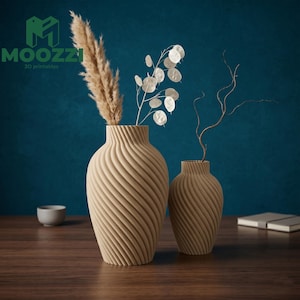 May include: Two beige, spiral-textured vases of different sizes, holding dried plants, sit on a wooden table. The larger vase contains a tall, feathery plant, while the smaller one holds a delicate branch. The background is a dark teal wall. The logo "MOOZZI 3D printables" is in the upper left.