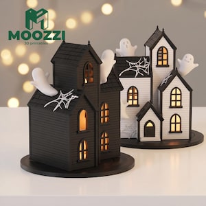 May include: Two miniature house structures, one black and one white, featuring arched windows with warm interior lighting. Each house is decorated with white spiderweb accents and small white ghost figures emerging from the roofs and sides.