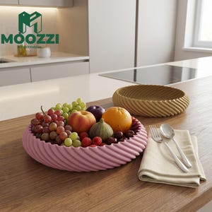 Może przedstawiać: Różowa miska na owoce z spiralnymi krawędziami wypełniona winogronami, malinami, pomarańczą i innymi owocami. Druga, podobna miska jest brązowa. Widelec, łyżka i serwetka leżą na drewnianej powierzchni. Logo "MOOZZI 3D printables" znajduje się w lewym górnym rogu.