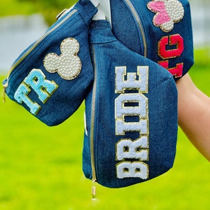 May include: Three denim fanny packs with white and gold lettering. The packs are decorated with a Mickey Mouse head, a pink bow, and the word "Bride".