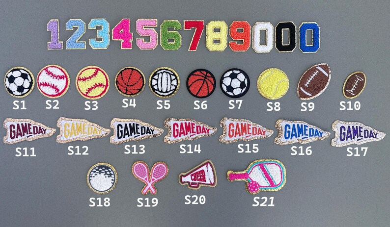 May include: A collection of embroidered patches featuring numbers, sports balls, and pennants. The patches include numbers 0-9, soccer balls, baseballs, basketballs, tennis balls, footballs, and pennants with "GAME DAY" text.