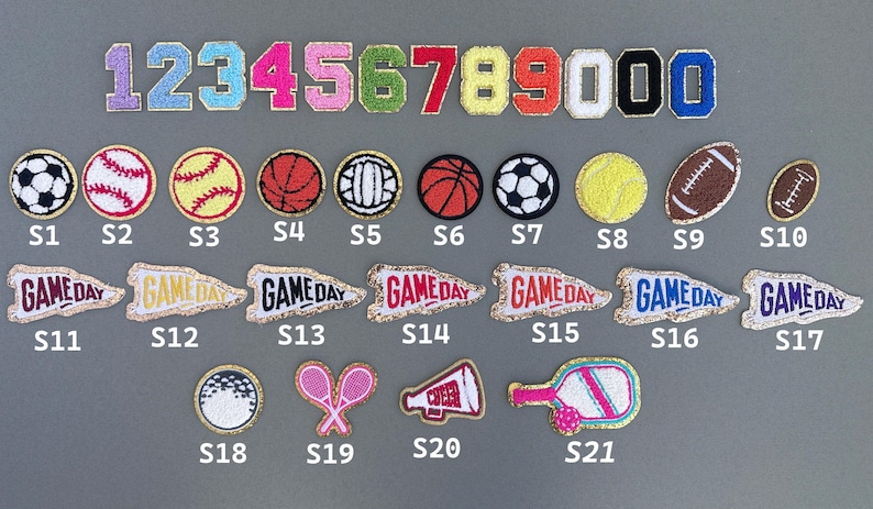 Op de afbeelding: Een verzameling geborduurde patches met sportballen, wimpels met de tekst "Game Day" en cijfers. Inclusief ontwerpen voor voetbal, tennis en basketbal. De patches zijn in verschillende kleuren.