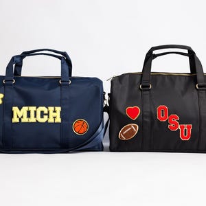以下が含まれることがあります： 2つのダッフルバッグ。1つは「MICH」の文字、バスケットボール、星、スマイリーフェイスが付いたネイビーブルー。もう1つは「OSU」の文字、ハート、フットボール、数字の3が付いた黒色です。