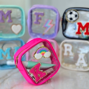 May include: A set of clear plastic zippered pouches with colorful accents. The pouches are decorated with letters, a rainbow, a lightning bolt, a heart, a soccer ball, and a cloud.