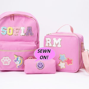 May include: Pink backpack, lunch bag, and pencil case with sewn-on patches and names "SOFIA" and "RM". The patches include a paw print, unicorn, stars, and a smiley face.