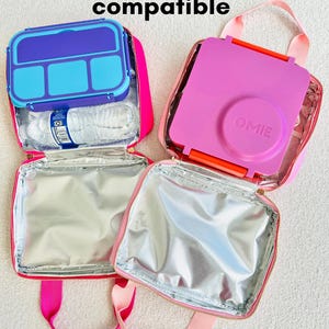 May include: Two Omie & Bento Box compatible lunch bags. One bag is open, showing a blue and purple bento box and a water bottle. The other bag is open, showing a pink bento box. The bags are pink with silver insulated interiors.