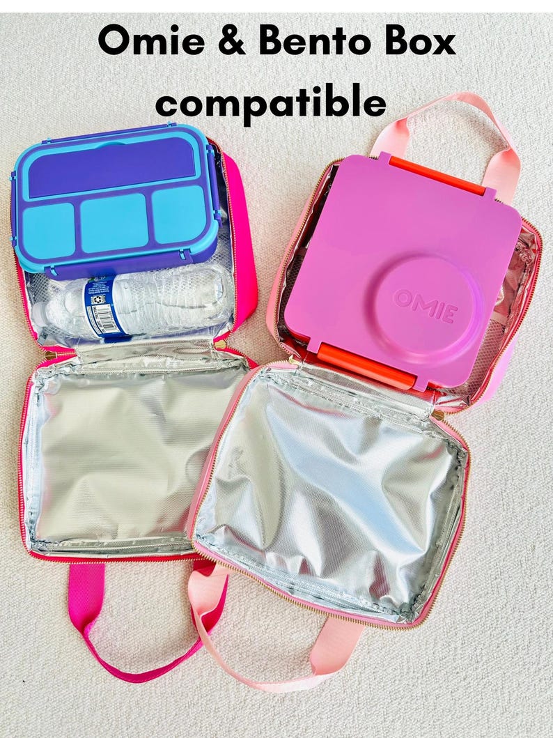 May include: Two Omie & Bento Box compatible lunch bags. One bag is open, showing a blue and purple bento box and a water bottle. The other bag is open, showing a pink bento box. The bags are pink with silver insulated interiors.