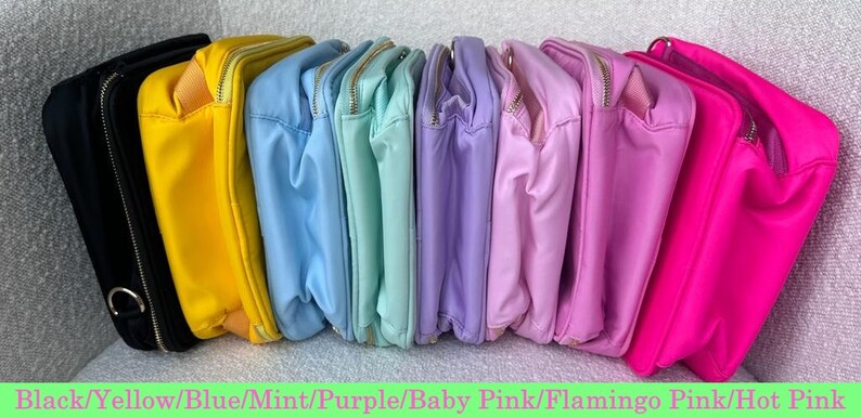 May include: A collection of colorful, rectangular pouches in various shades, including black, yellow, blue, mint, purple, baby pink, flamingo pink, and hot pink. Each pouch has a gold zipper and a matching interior lining.