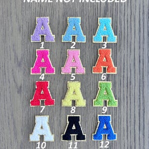May include: Twelve embroidered letter "A" patches in a range of colours, such as purple, blue, pink, orange, red, yellow, green, white, black, and blue. Each patch has a gold border and is numbered from 1 to 12.